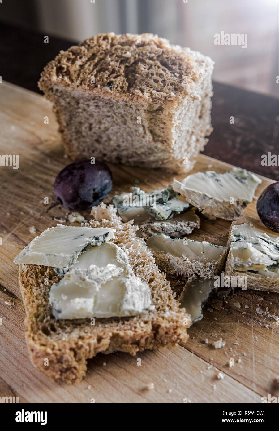 Su una tavola di legno è possibile vedere una fetta di pane rustico, briciole, qualche formaggio blu e due uve. Foto Stock