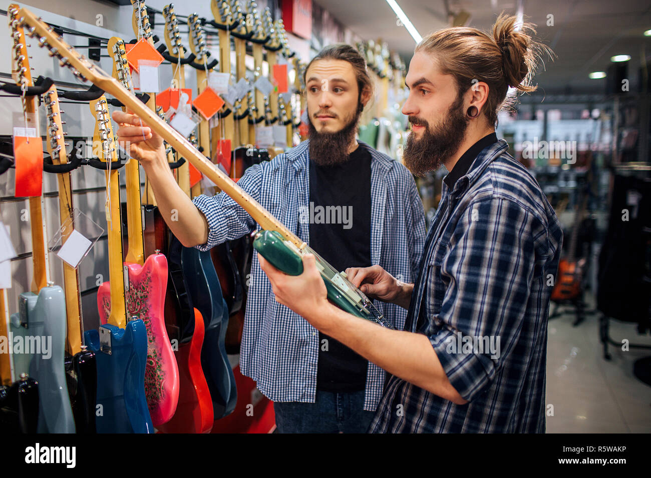 Due musicisti di stare in piedi insieme alla fila di chitarra. Un giovane uomo tenere la chitarra bianca tocca un altro suo bar. Essi vengono in negozio per chitarra Foto Stock