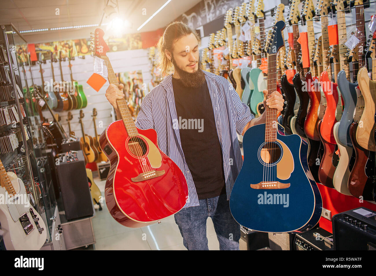 Foto di giovani hipster stand e tenere due coloratissimi chitarre acustiche. Essi sono di colore rosso e blu scuro a colori. Guy guardare al secondo. L'uomo chitarre elettriche Foto Stock