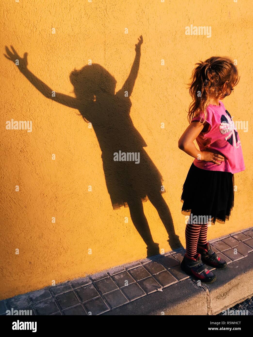 Ragazza in piedi con le mani sui suoi fianchi e il suo alter ego ombra con le mani in aria Foto Stock