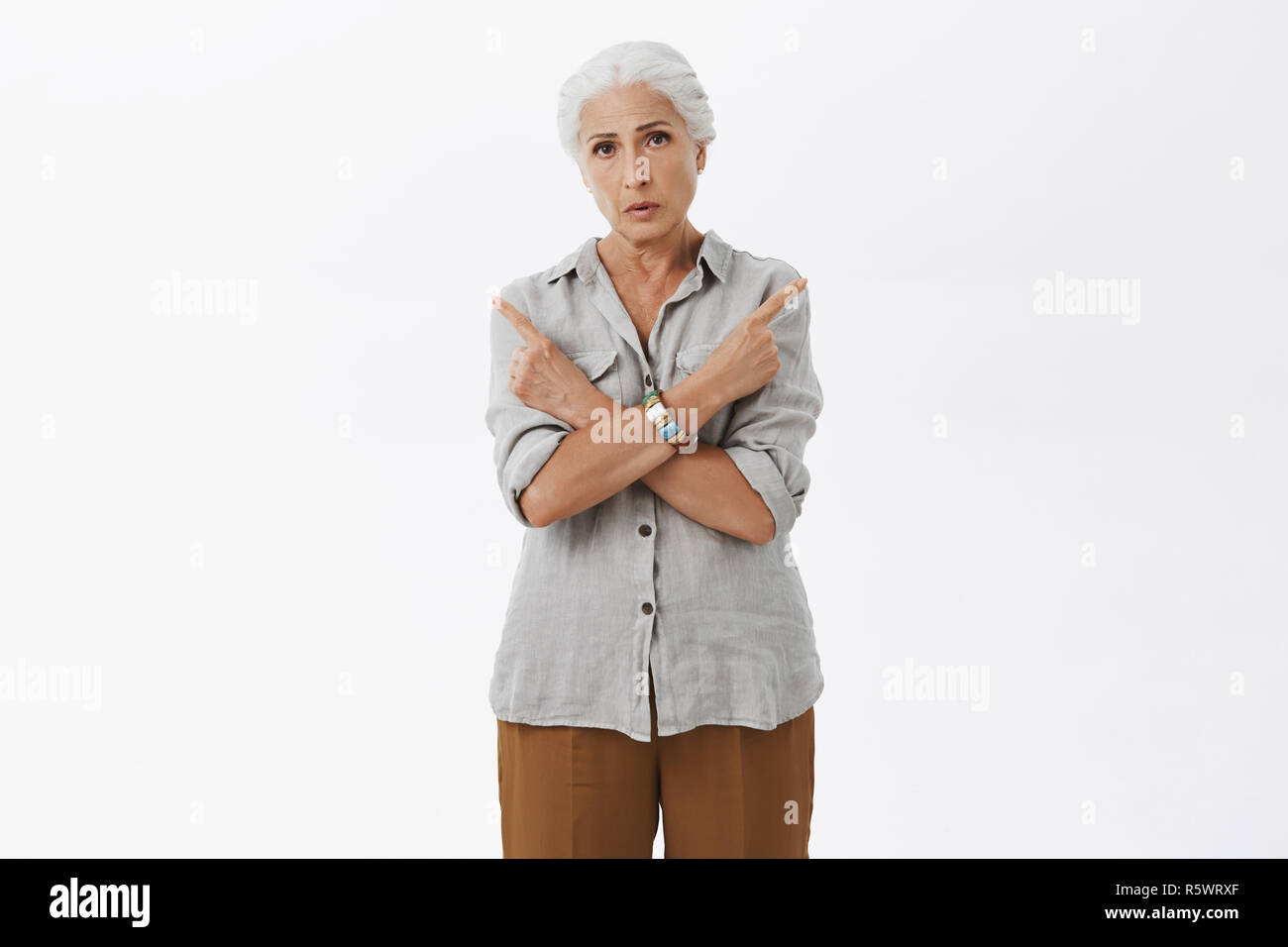 Vecchia donna non può decidere in quale modo migliore. Ritratto di confuso certi nonnina con i capelli grigi in camicia casual bracci di incrocio sul petto rivolta verso sinistra e R Foto Stock