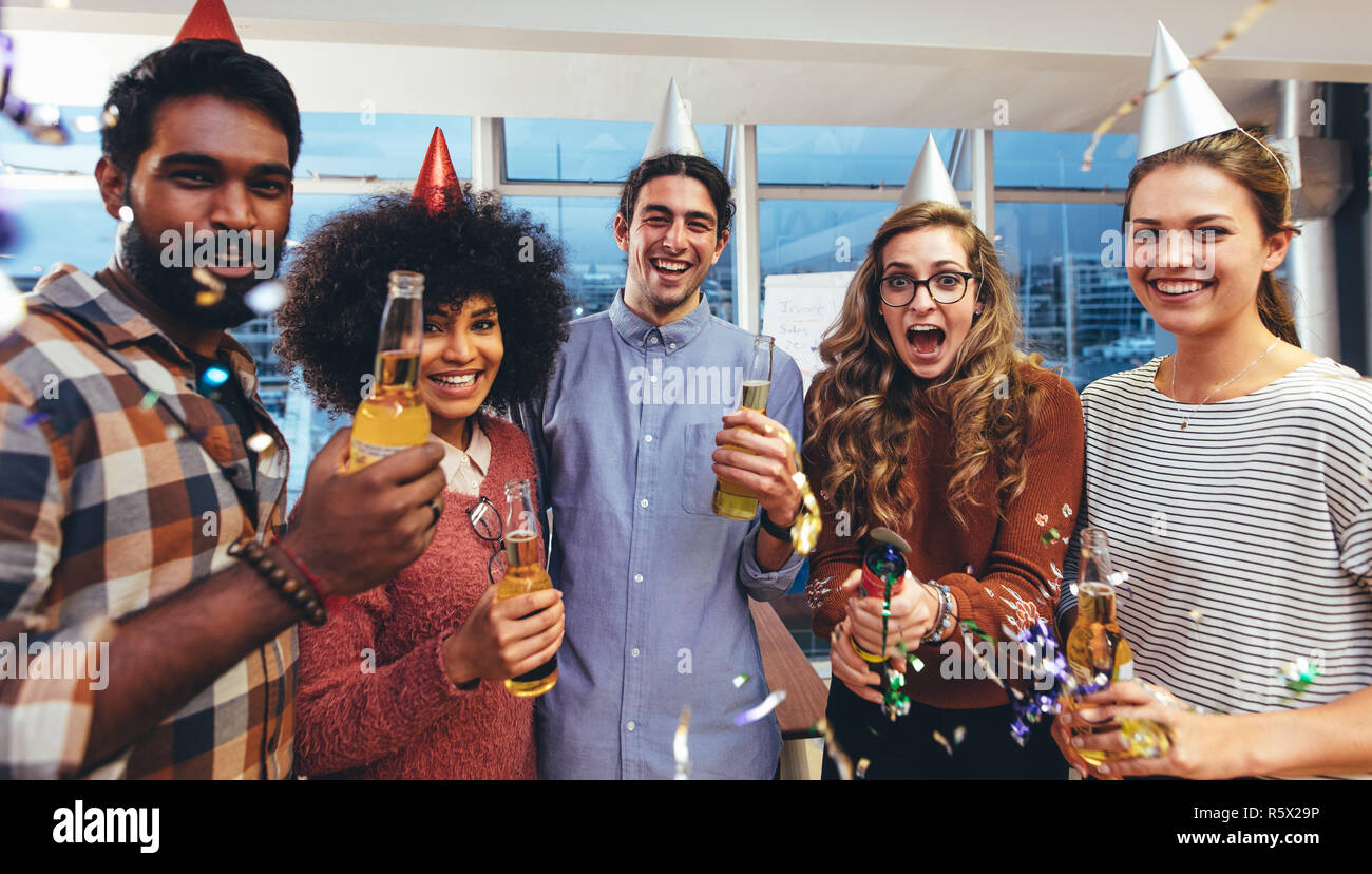 Sorridendo gli uomini e le donne in parte i cappucci e tenendo la birra godendo di un partito. I colleghi divertirsi a una festa in ufficio per festeggiare il successo. Foto Stock