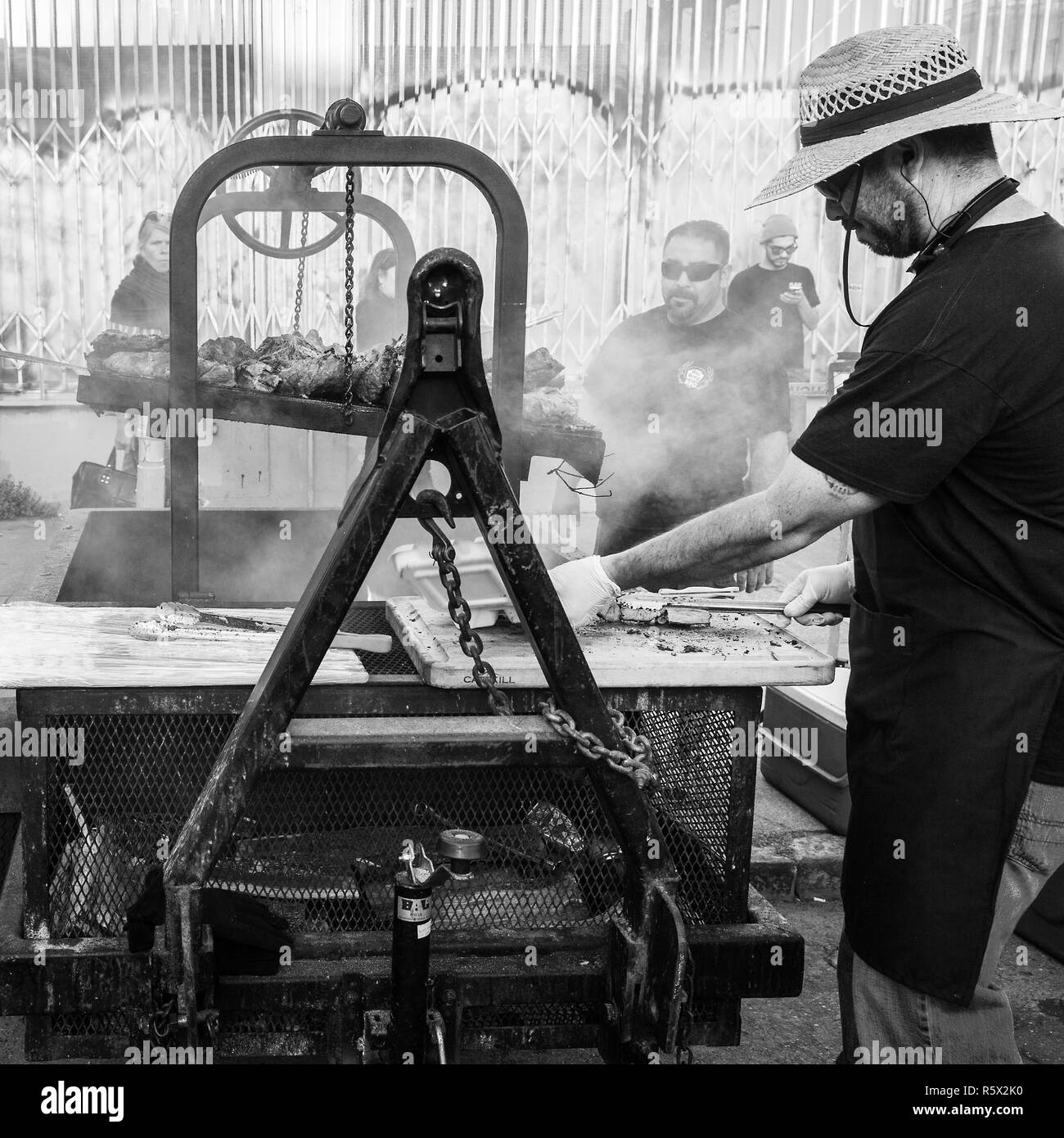 OAKLAND, CA-Giugno 6, 2014: Street chef in arte mormorio cuochi il barbecue su una forza industriale grill. Il grintoso urbano. In bianco e nero di formato quadrato. Foto Stock