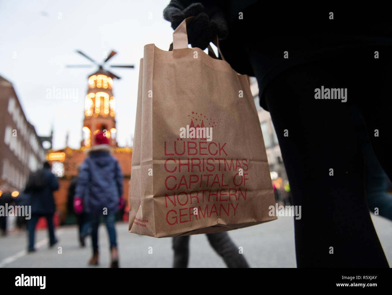 01 dicembre 2018, Schleswig-Holstein, Lubecca: una donna è in possesso di una carta borsa di trasporto con la scritta 'Lübeck capitale di Natale della Germania del Nord' presso il mercatino di Natale nel centro della citta'. Meno rifiuti in plastica - questa tendenza è anche previsto per prevalere a mercati di Natale. Sui mercati del nord vi è il punzone da tazze di ceramica. Nuova carta sono sacchi da asporto per piccoli acquisti natalizi, che sono stati distribuiti a tutti dello spettacolo da Lubecca e Travemünde Marketing (LTM) con l'iscrizione "Lübeck - Città natale del Nord' e la traduzione inglese 'Lübeck capitale di Natale di Northe Foto Stock