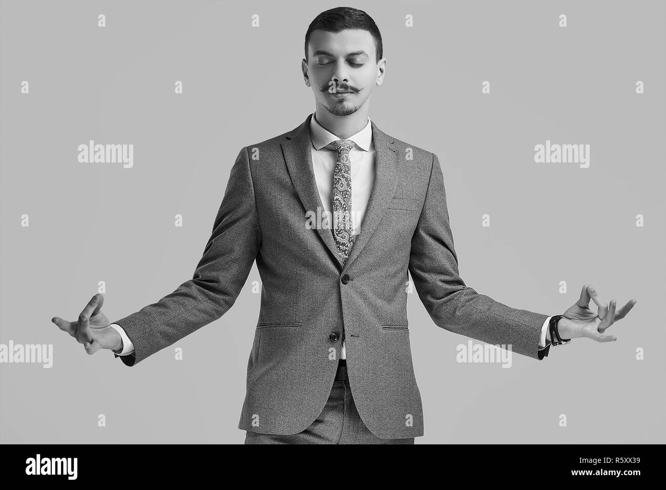 Ritratto di bel giovane fiducioso arabo imprenditore con baffi di fantasia in moda grigio tuta completa meditando di sfondo per studio Foto Stock