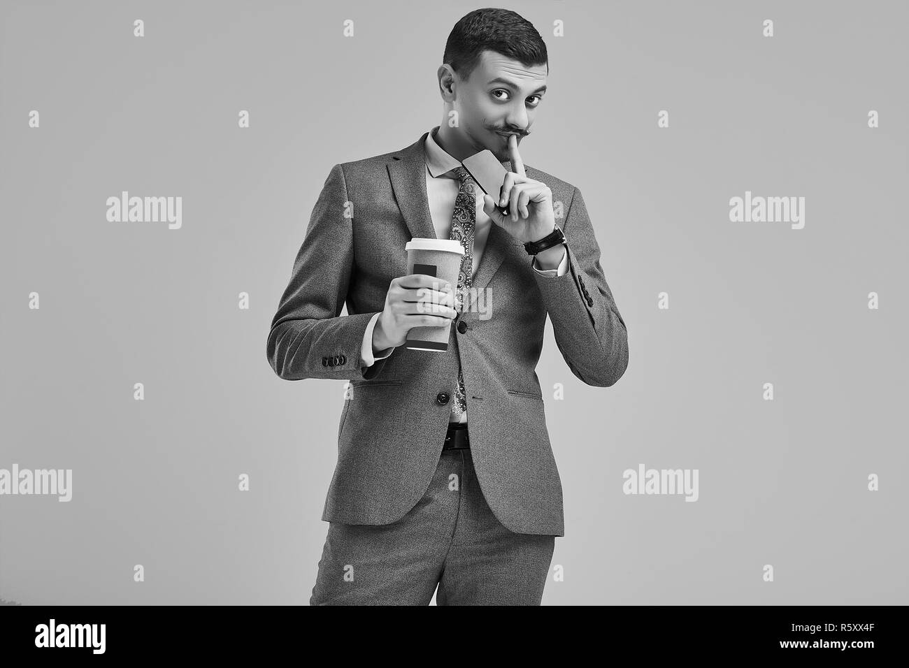 Ritratto di bel giovane fiducioso arabo imprenditore con baffi di fantasia in moda grigio tuta completa contiene una tazza di caffè nelle sue mani su studio bac Foto Stock