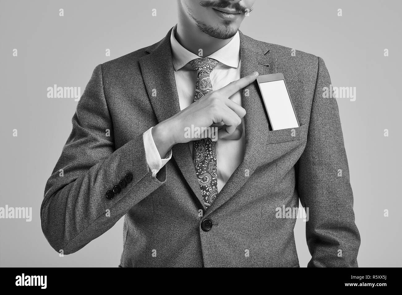 Close-up verticale del bel giovane fiducioso arabo imprenditore con baffi di fantasia in moda grigio tuta completo Nascondere il telefono in tasca su studi Foto Stock