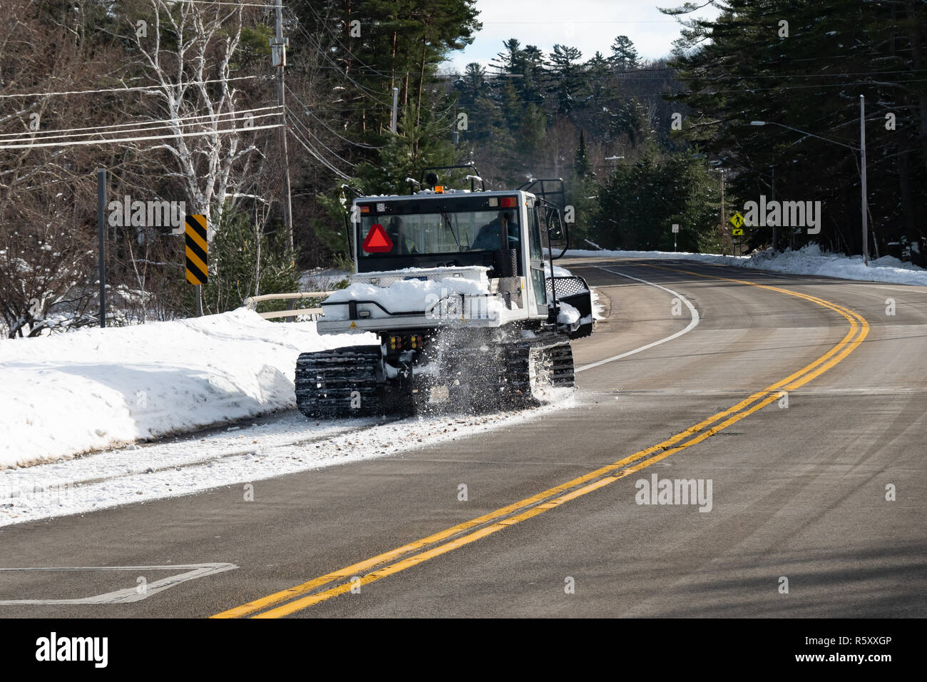 Un Prinoth Husky groomer neve la guida verso il basso il lato dell'autostrada per attraversare un ponte in speculatore, NY USA parte di una motoslitta trail. Foto Stock