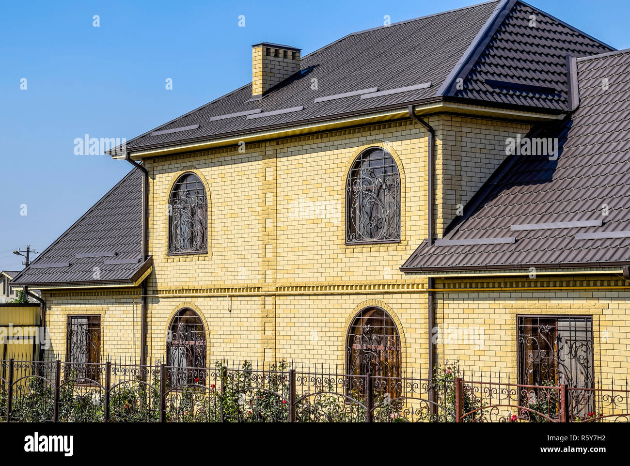 Casa del mattone giallo e marrone e tetto ondulato in metallo. Tralicci su windows. Foto Stock