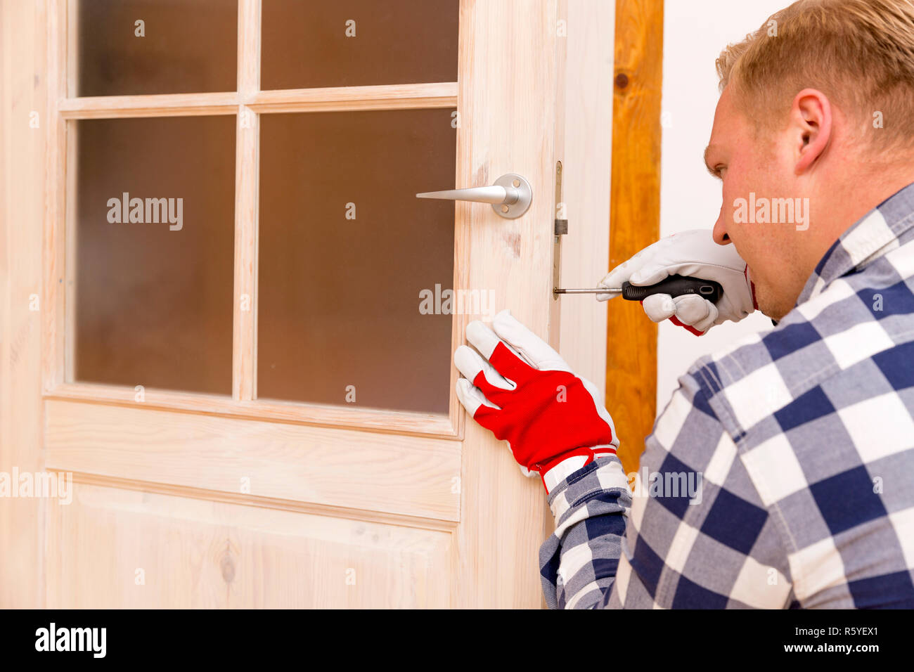 Tuttofare che fissa la porta con un cacciavite Foto Stock