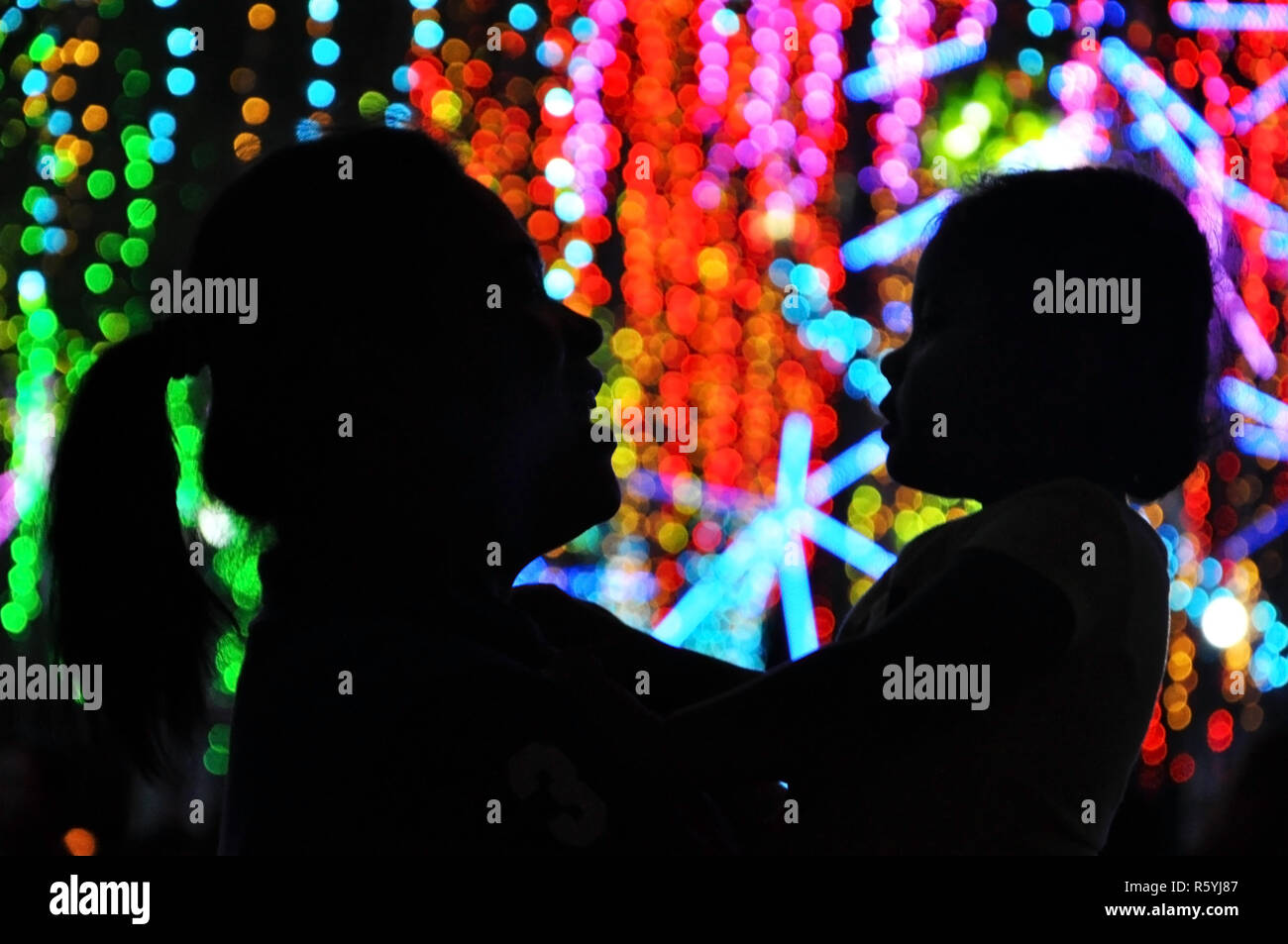 Una madre e figlia si stagliano da colorate le luci di Natale di cui godono le luci di Natale la visualizzazione in Makati City, Filippine. Foto Stock