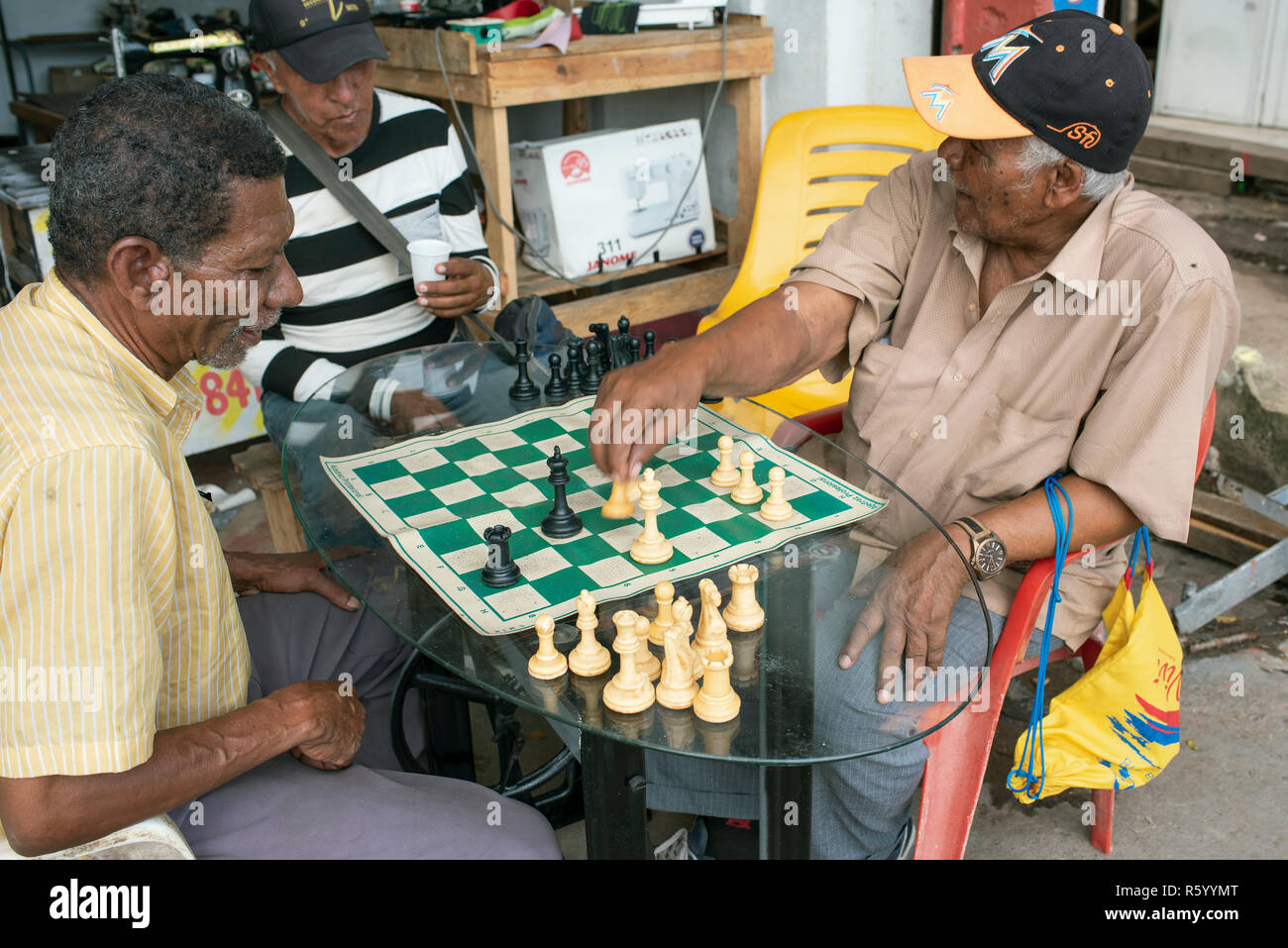 Afro-Colombian uomini giocare a scacchi al di fuori di una macchina da cucire repair shop. Lo stile di vita quotidiano in Cartagena de Indias, Colombia. Ott 2018 Foto Stock