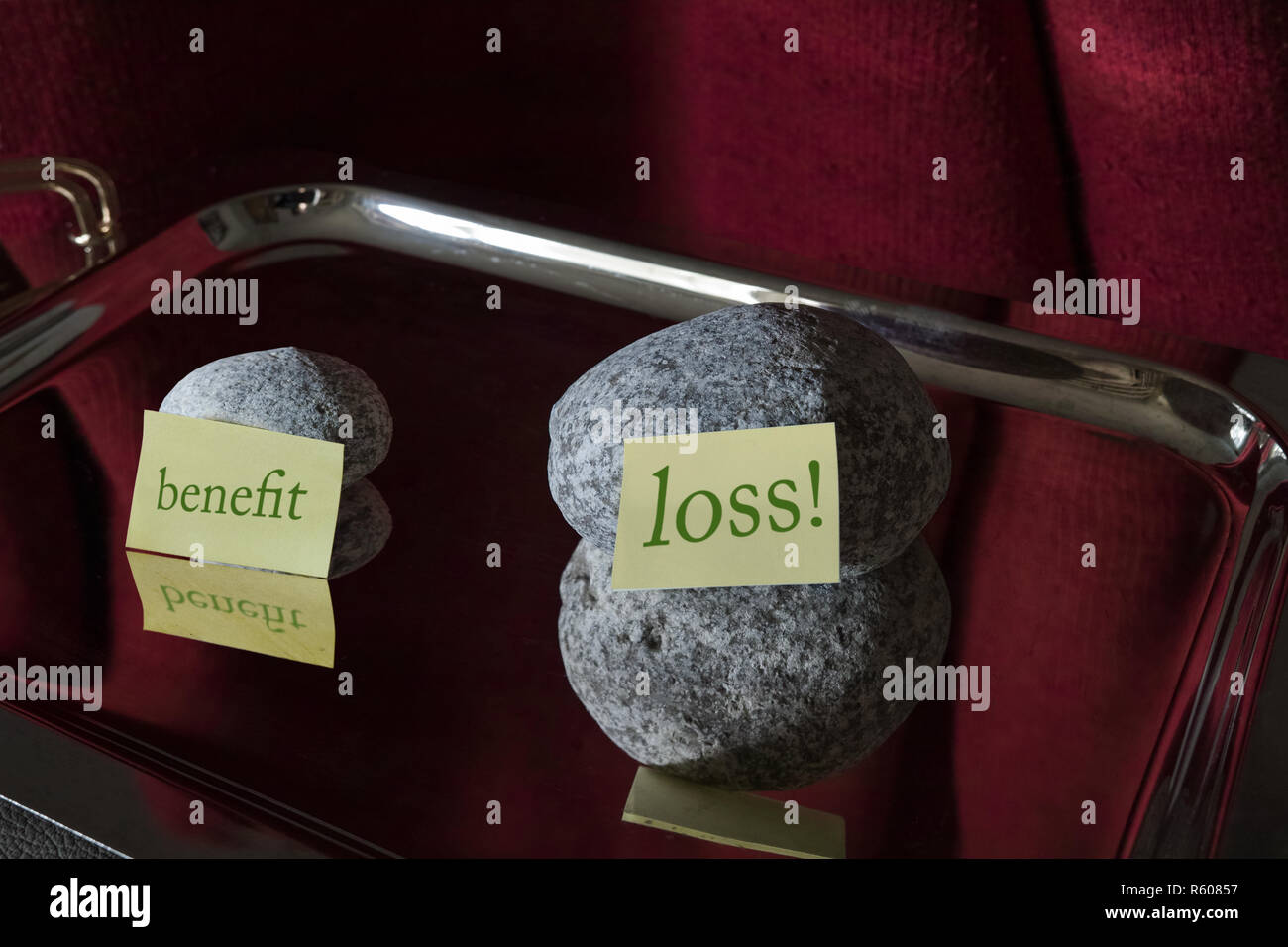 Due pietre su un piatto d'argento. Una più grande con un post-it di fronte si dice "perdite", una più piccola con un post-it nella parte anteriore dove si dice "vantaggio". Foto Stock