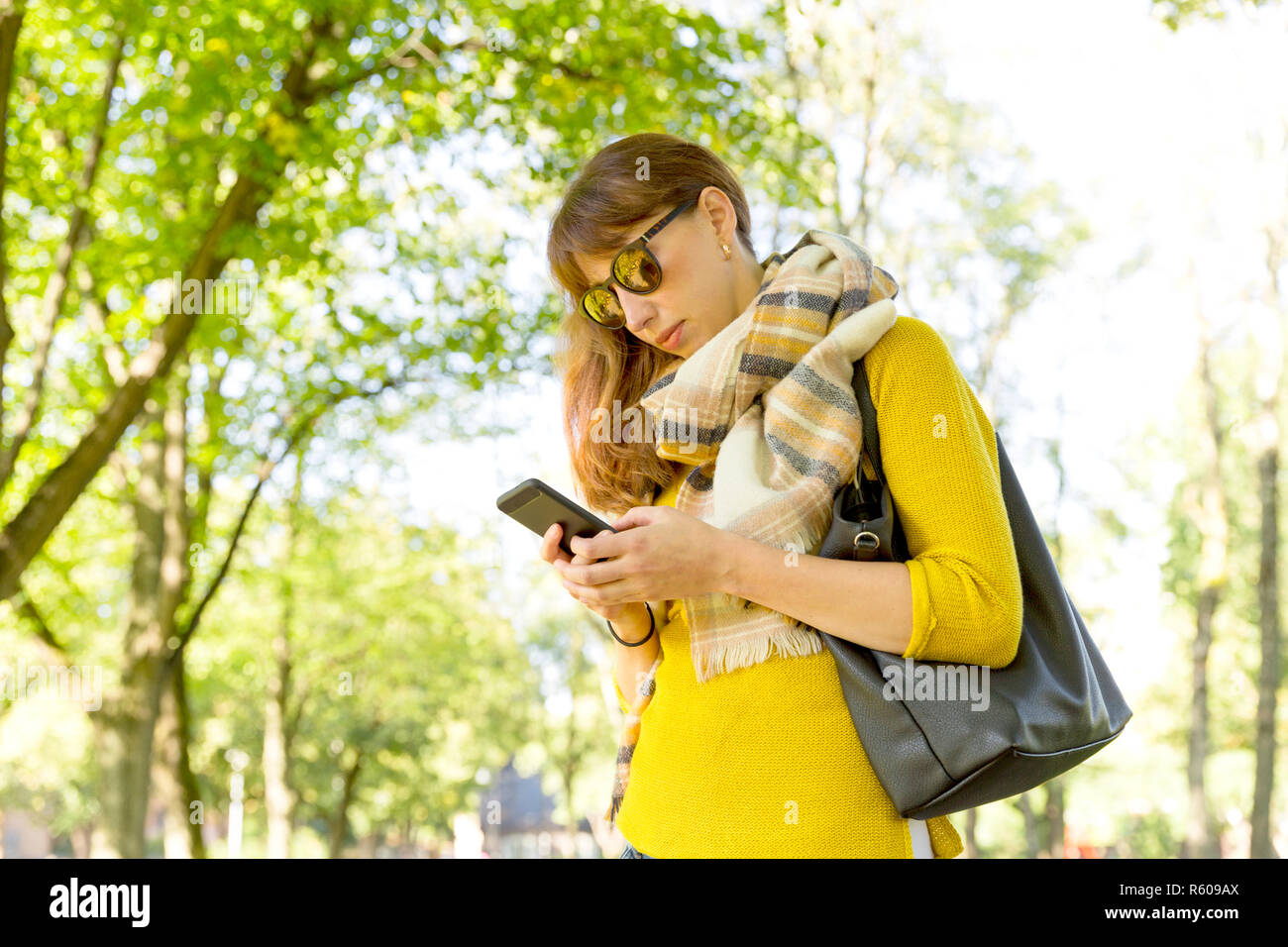 Carino donna è piacevole la lettura di un messaggio di testo sul telefono cellulare durante una passeggiata nel parco in autunno caldo giorno Foto Stock