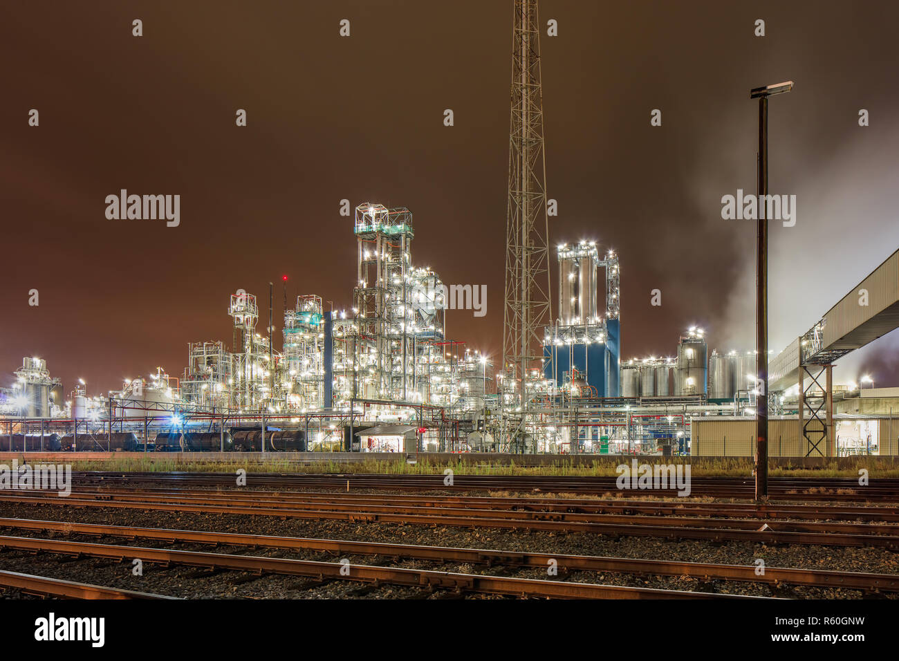 Scena notturna illuminata con produzione petrolchimica pianta con binari del treno di fronte ad Anversa, Belgio. Foto Stock