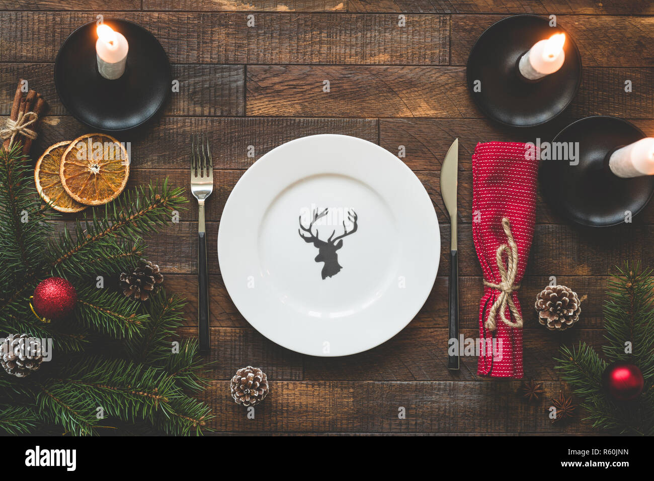 Natale messa in tavola con piastra vuota, argenteria, candele accese, tabella rossa sul tessile tavola in legno rustico. Vista superiore, copia spazio per il testo. Beauti Foto Stock