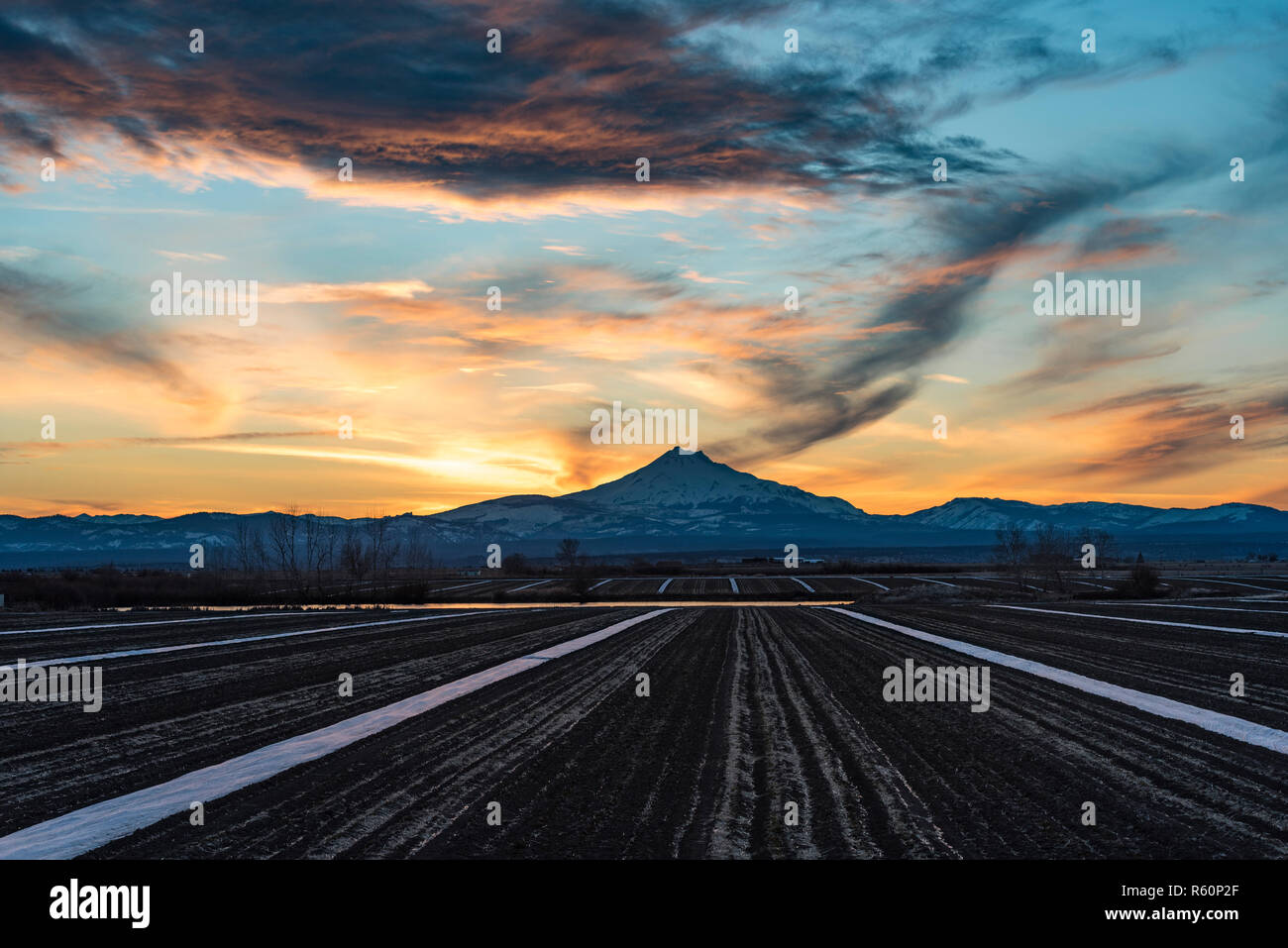 I campi agricoli con il Bianco di linee rette, montagne coperte di neve e drammatico il cielo al tramonto Foto Stock