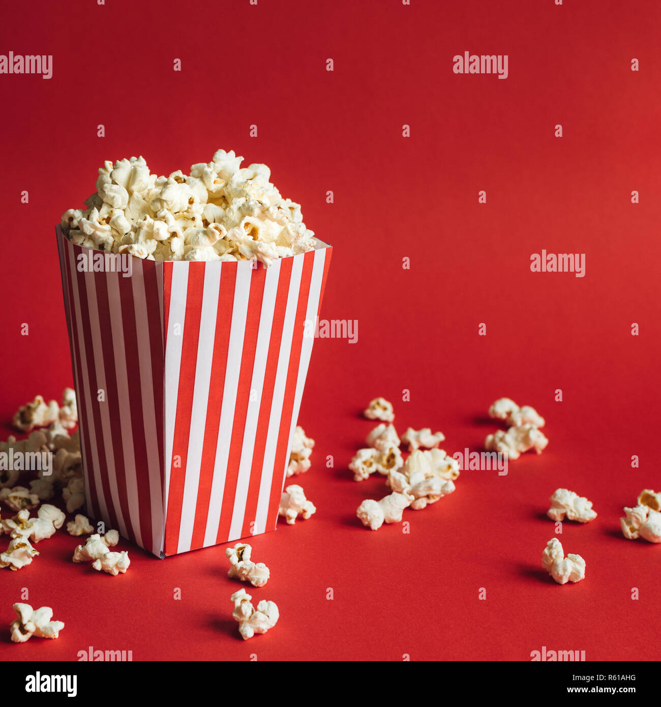 Scatola a strisce con popcorn su sfondo rosso. Formato quadrato Foto Stock