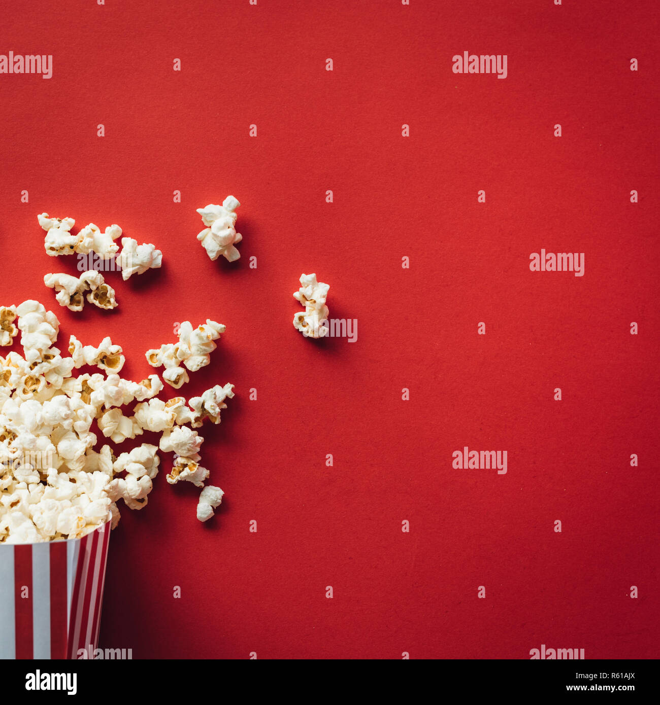 Scatola a strisce con popcorn su sfondo rosso. Formato quadrato Foto Stock