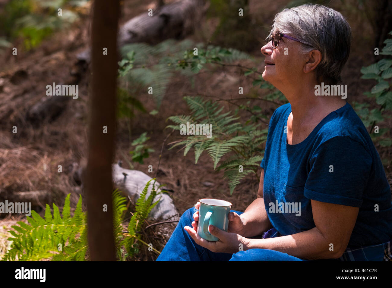 Matura donna caucasica sedersi nella foresta cercando il luogo e bere una tazza di tè o caffè - Concetto di riposo per le persone che amano viaggiare e scoprire Foto Stock