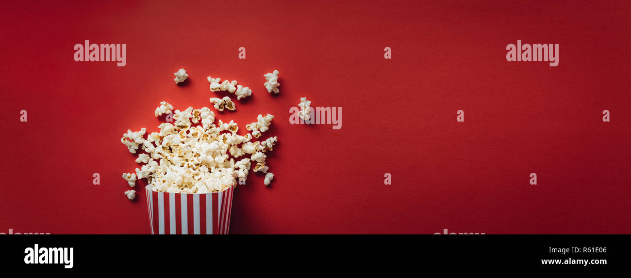 Scatola a strisce con popcorn su sfondo rosso. Formato wide, banner Foto Stock