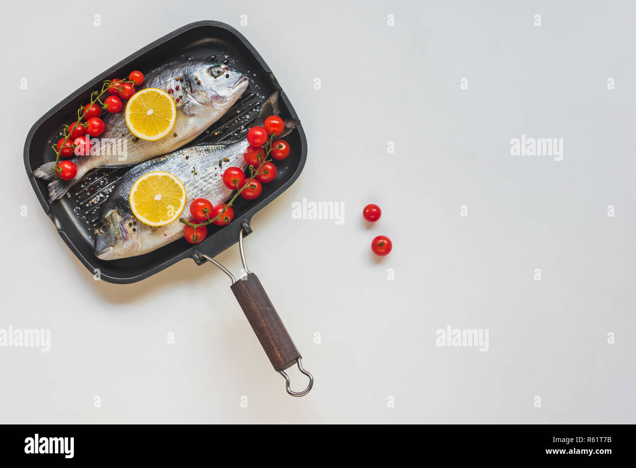 Vista superiore del pesce crudo decorata da limone e pomodori ciliegia nel vassoio da forno Foto Stock