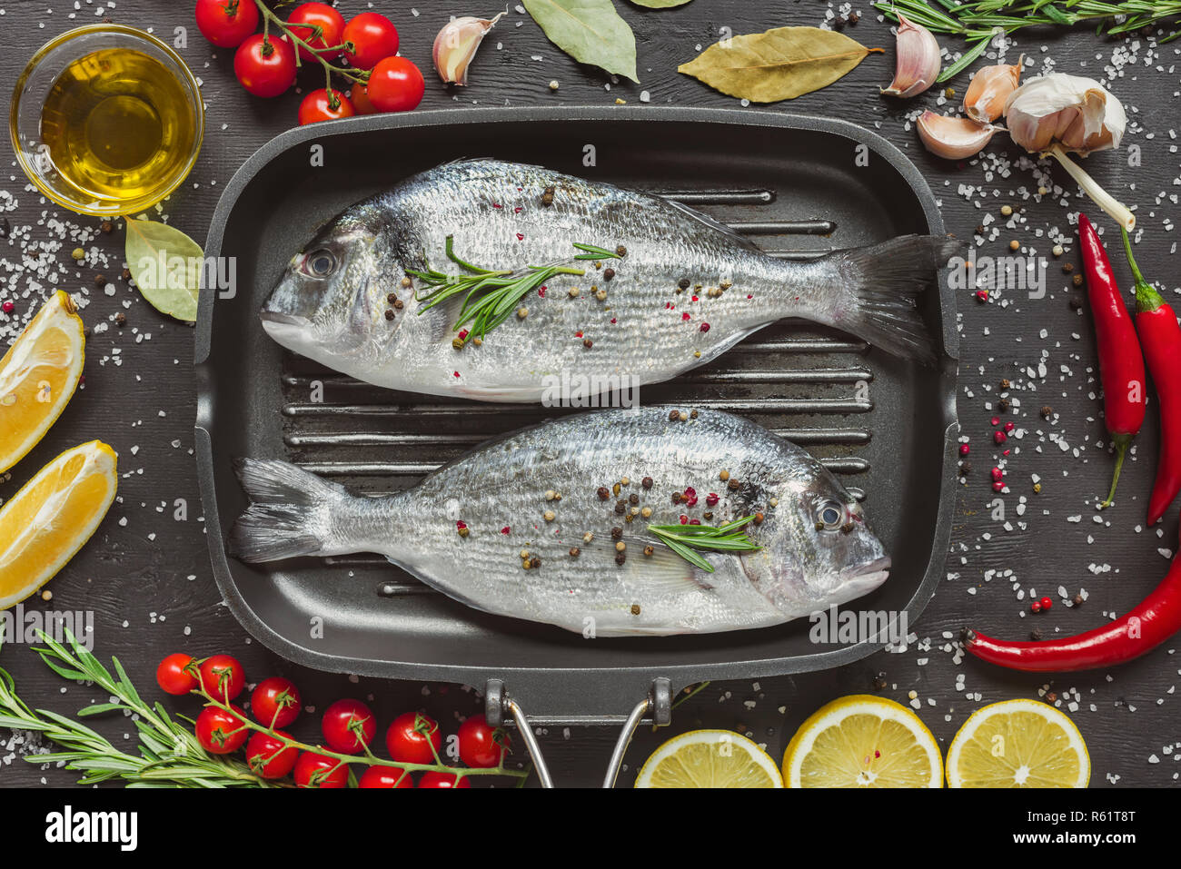 Vista da sopra del pesce crudo nel vassoio da forno circondato da ingredienti sulla tavola nera Foto Stock