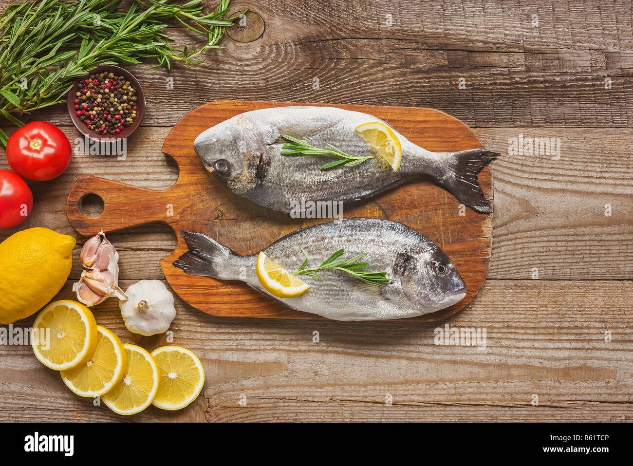 Vista superiore del pesce crudo su tavola di legno con rosmarino e limone sul tavolo Foto Stock