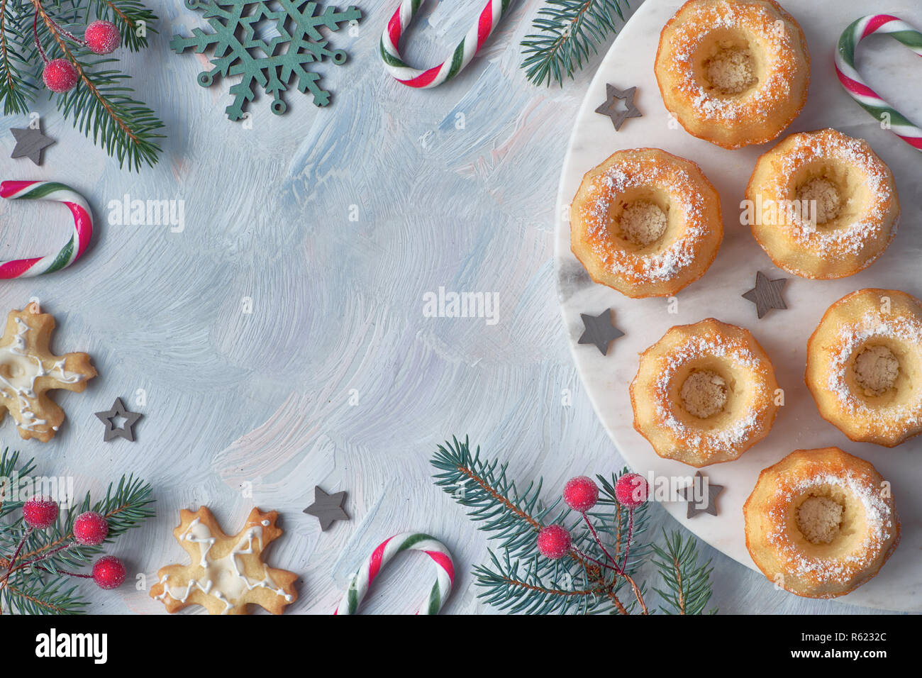 Mini anello bundt torte con lo zucchero a velo su sfondo chiaro con ramoscelli di abete, le bacche e le canne di caramella. Vacanze di Natale cibo dolce, laici piatta con testo s Foto Stock
