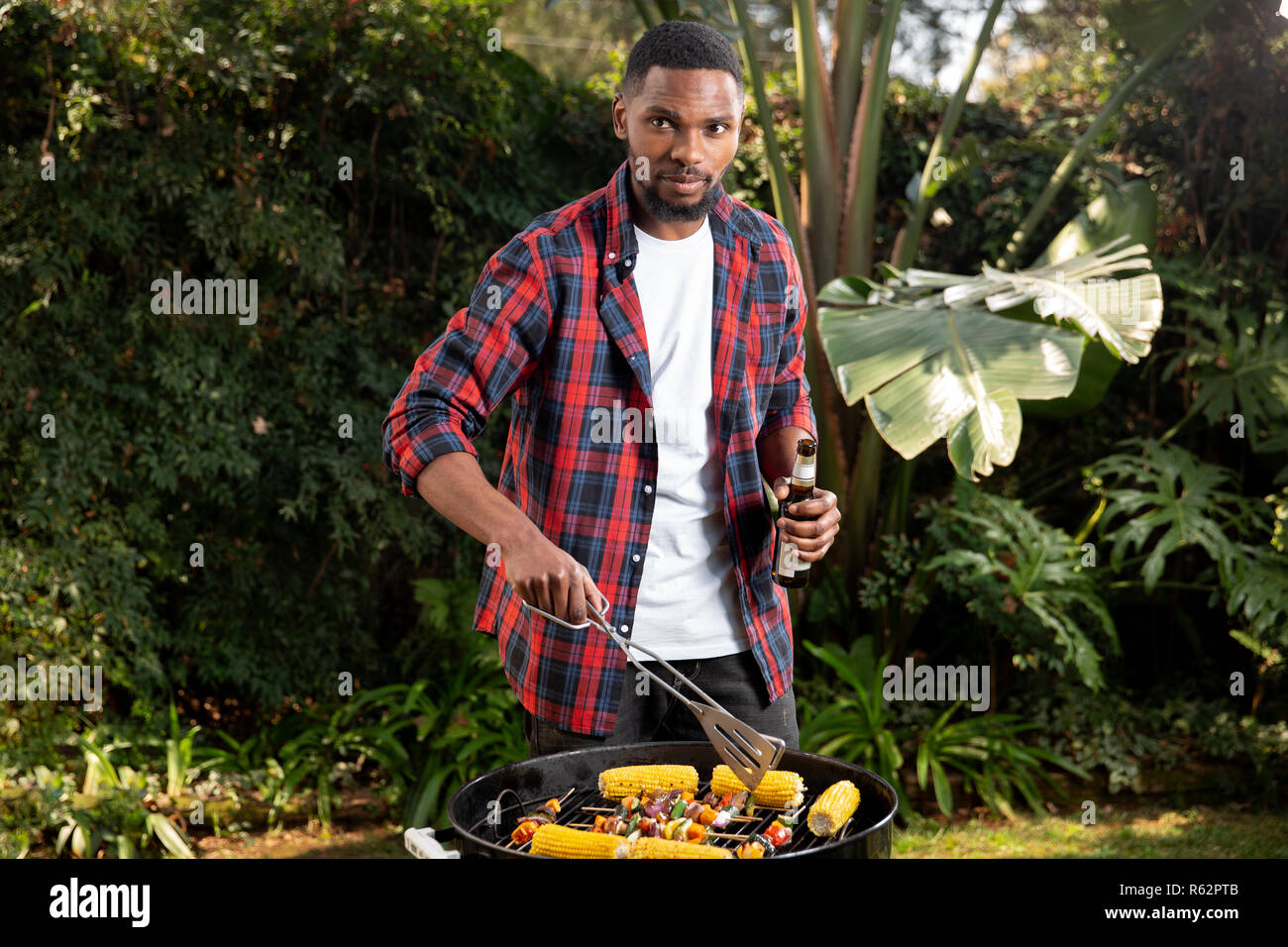 Un uomo con una birra e verdure alla brace Foto Stock