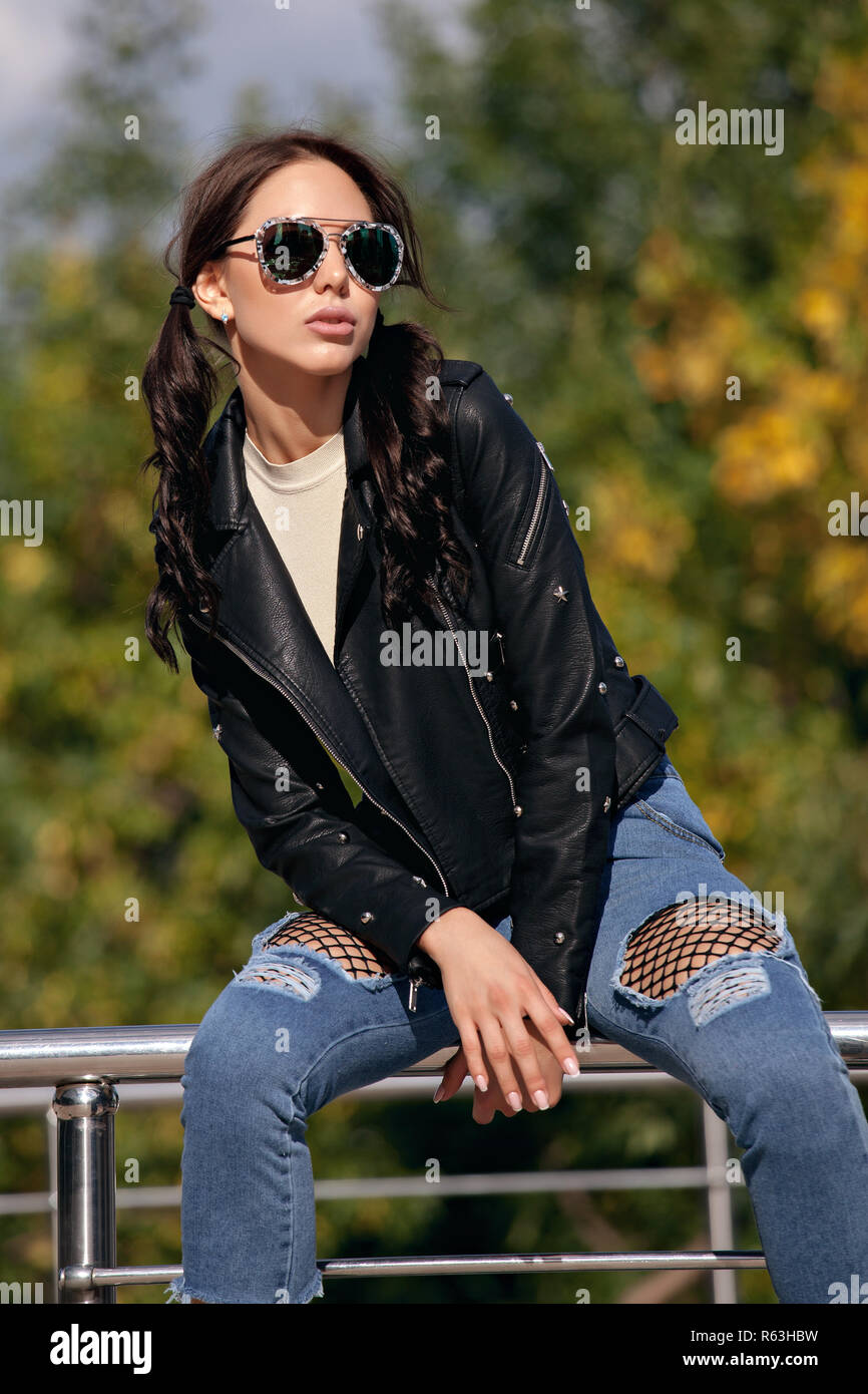 Moda giovane donna in stile rock vestiti, nero giacca di pelle, blue jeans,  collant in una griglia sotto martoriata jeans Foto stock - Alamy