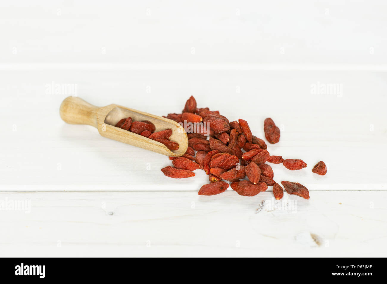 Sacco di essiccato intero red goji bacche con cucchiaio in legno su legno bianco Foto Stock