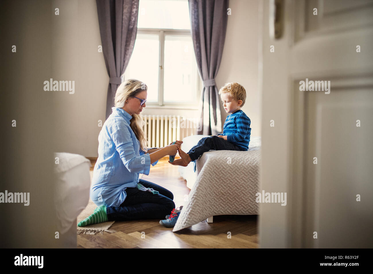 Una giovane madre di mettere i calzini sul bambino figlio all'interno di una camera da letto. Foto Stock