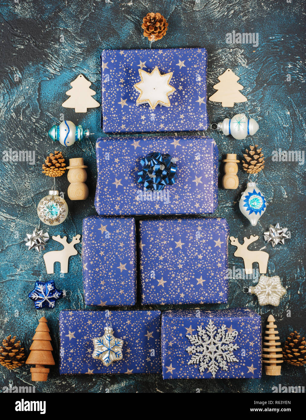 Creative Chritmas composizione. Presenta in carta blu con brillantini argento, decorazioni in legno, ornamenti, baubles disposti in forma di Natale tre Foto Stock