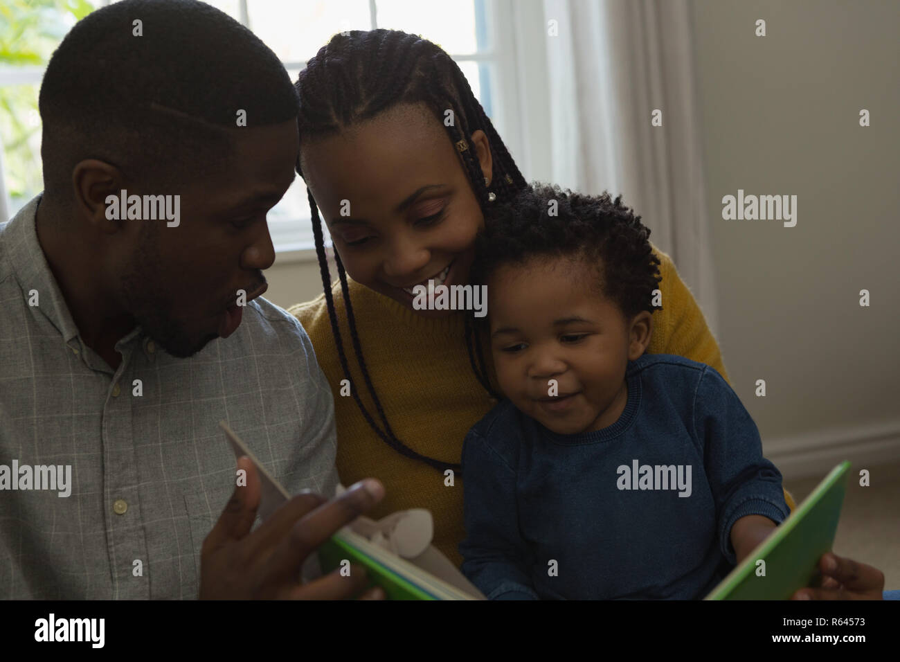 I genitori la lettura di un libro di fotografia con il loro figlio in una stanza vivente Foto Stock