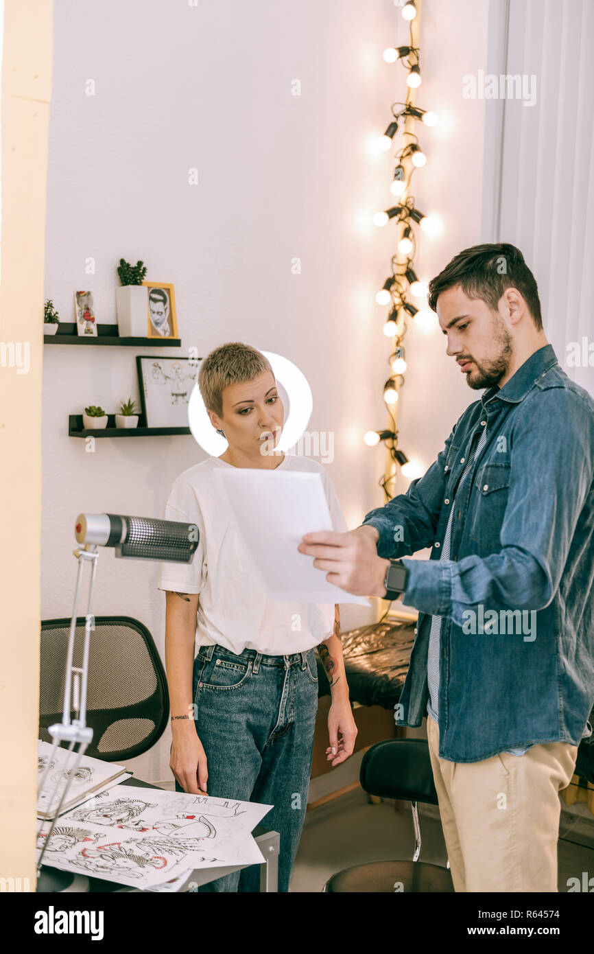 Tatuaggio femmina master con taglio di capelli fanciullesco attentamente guardando sulla foto Foto Stock