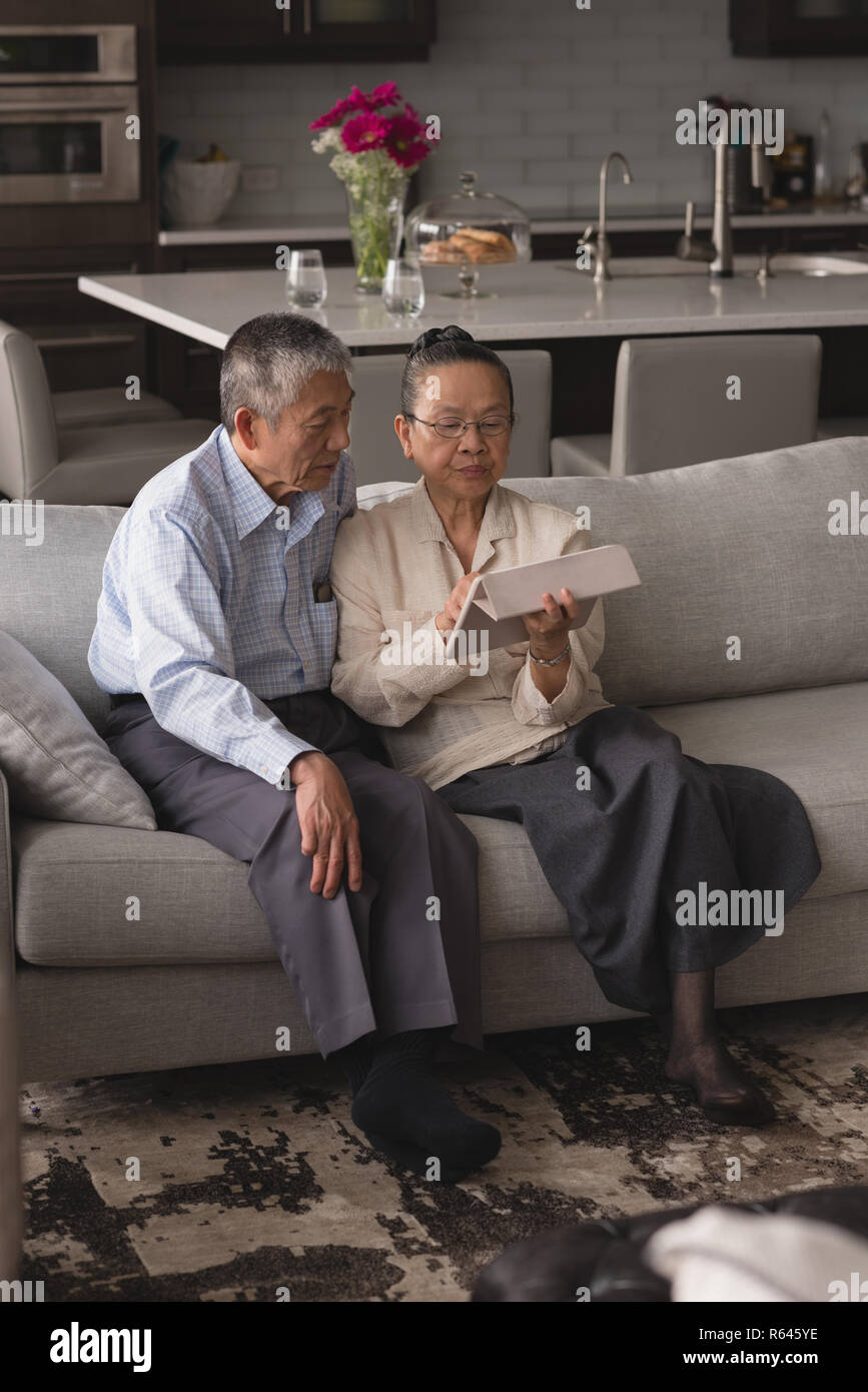 Coppia senior a discutere su una tavoletta digitale sul divano nel soggiorno Foto Stock