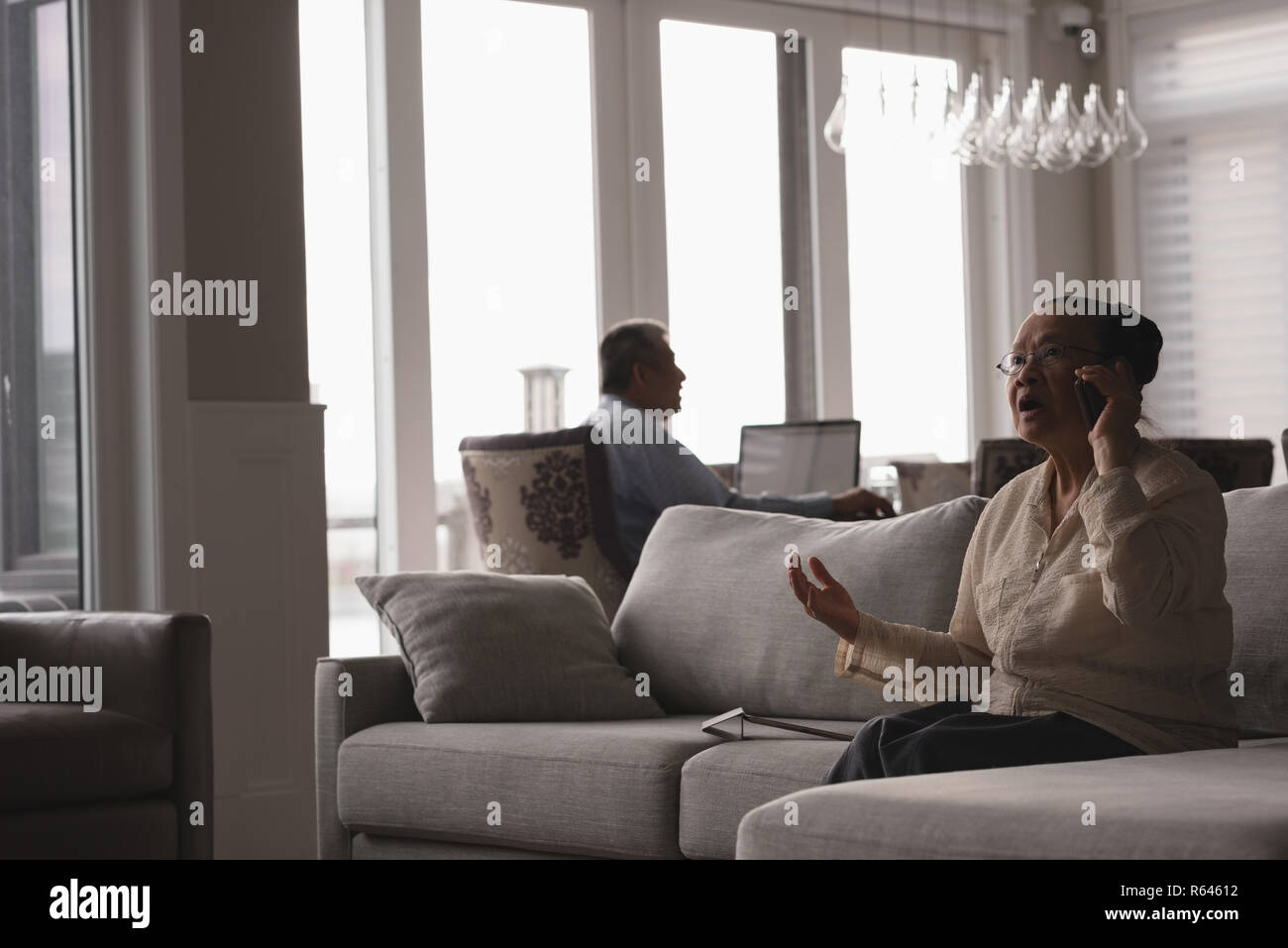 Senior donna parlando al telefono cellulare sul divano nel soggiorno Foto Stock
