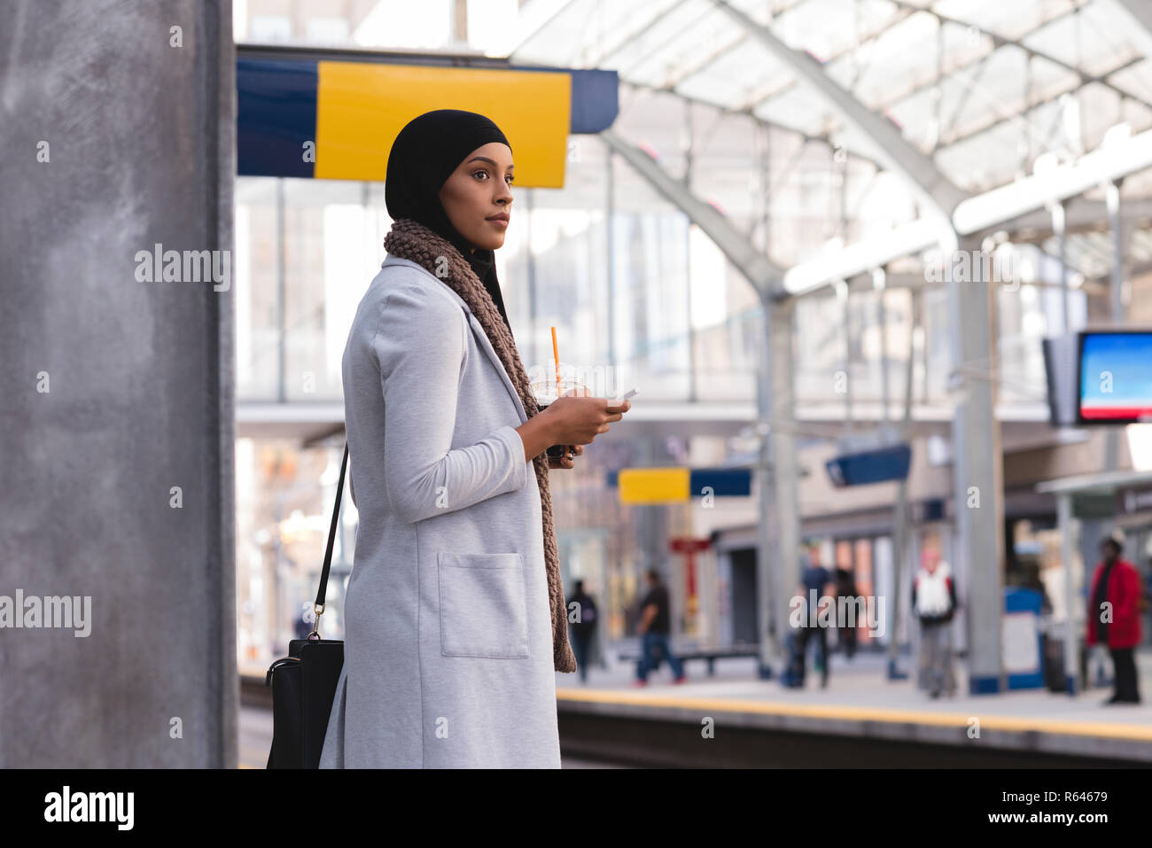 La donna in attesa del treno mentre si utilizza il telefono cellulare alla stazione ferroviaria Foto Stock