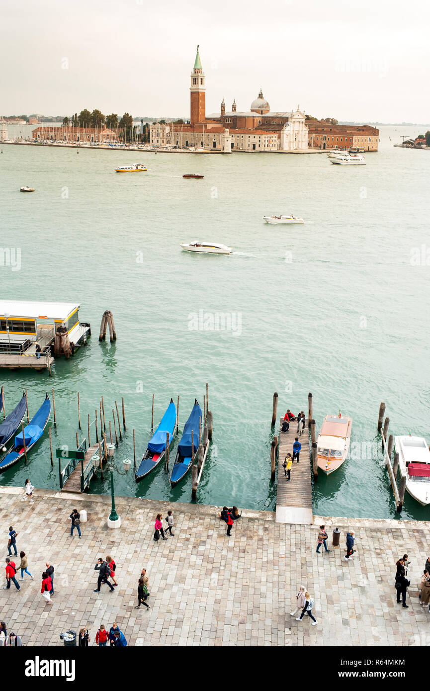Vista di San Giorgio isola dalla distanza attraverso acqua con barche. I turisti a piedi sul terrapieno della porta in primo piano Foto Stock
