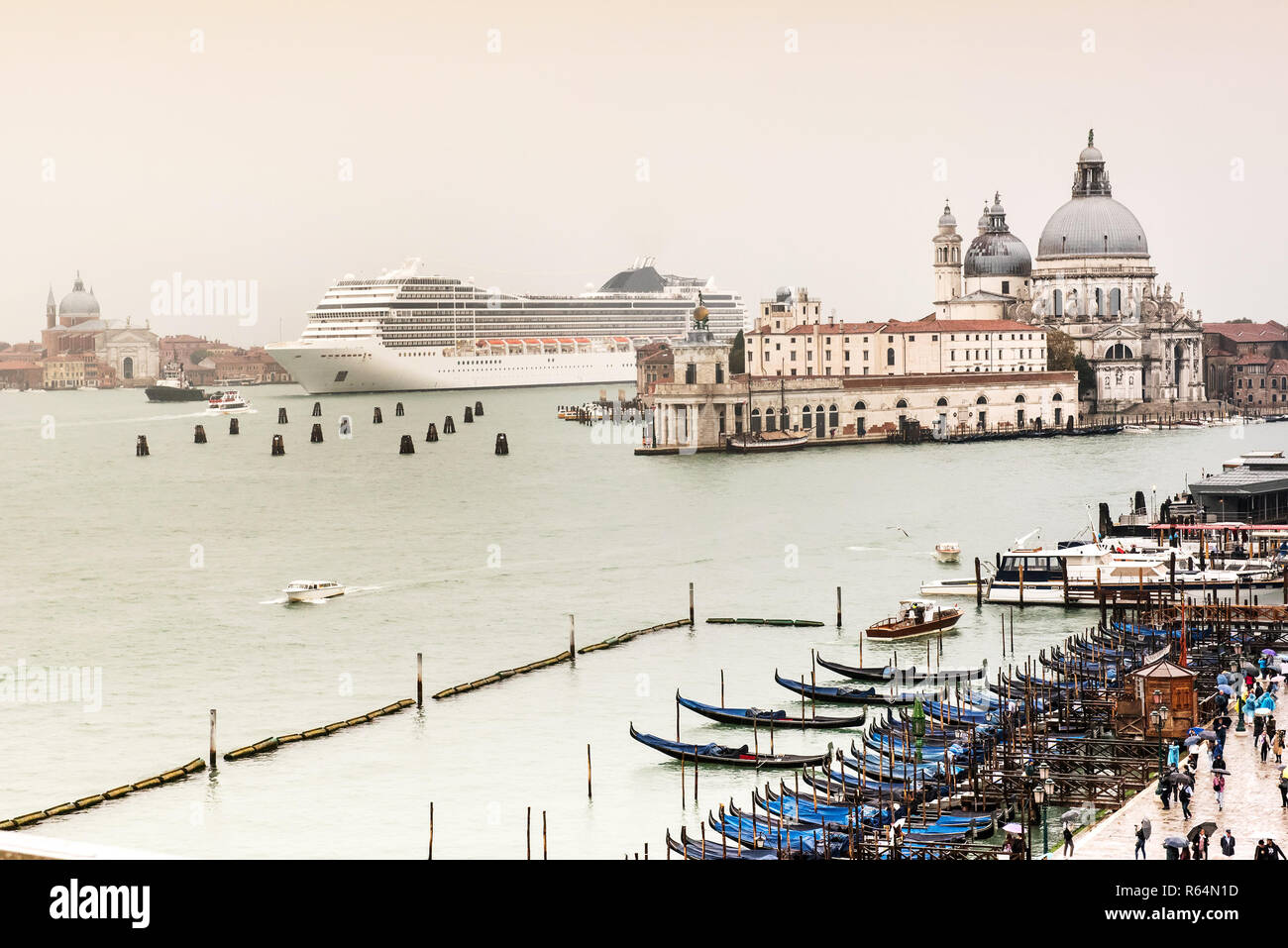 Bianco grande nave da crociera che arrivano a Venezia, Italia. Mostra la scala in contrasto con architettura locale e piccole imbarcazioni in primo piano. Giorno nuvoloso con cielo grigio Foto Stock