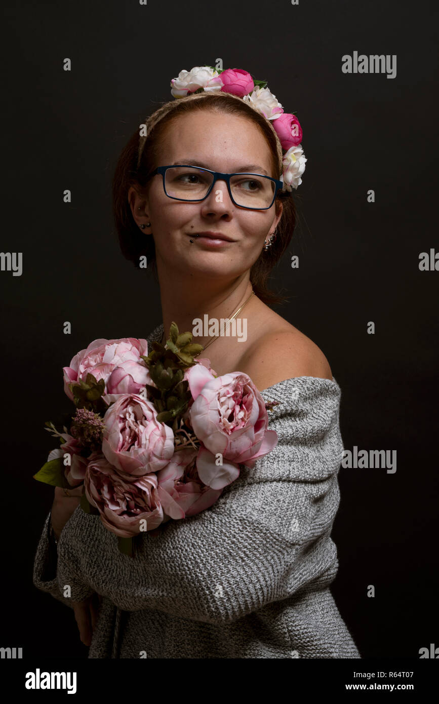 Ritratto di giovane donna che indossa occhiali, fiori di contenimento. Stile casual con un tocco femminilità Foto Stock