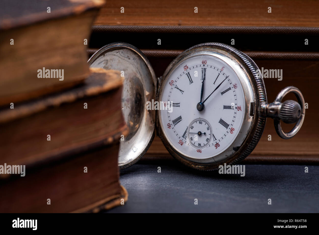 Panta Rhei concetto: antico orologio da tasca e la pila di vintage hard cover libri sulla pietra naturale dello sfondo. Foto Stock