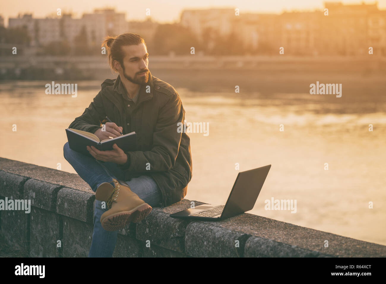 Bel uomo d affari l'uso di personal organizer e laptop mentre è seduto sul fiume. Foto Stock