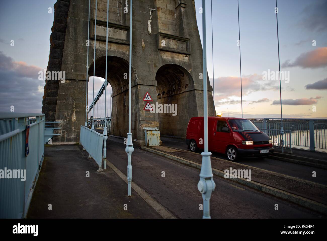 Un rosso VW Transporter van attraversa il Menai Suspension Bridge all'alba, Bangor, Gwynedd, Wales, Regno Unito Foto Stock