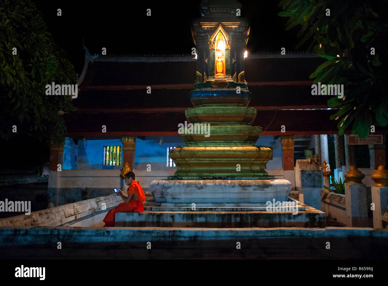 Giovane Monaco con un telefono cellulare in Wat Sensoukaram tempio buddista in Luang Prabang città Laos Foto Stock