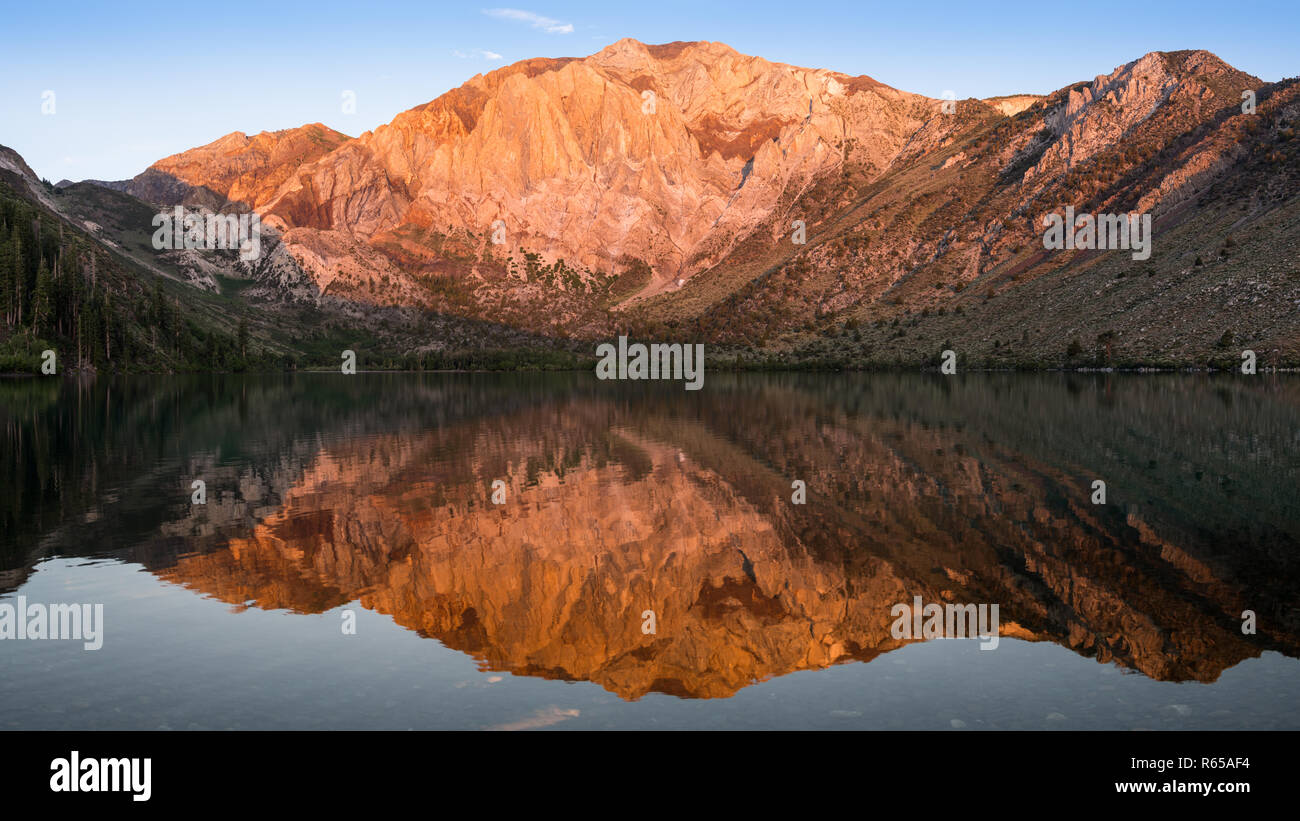 Panorama della luce dorata del tramonto sulle cime delle montagne si riflette nelle calme acque del lago trusty nelle montagne della Sierra Nevada della California Foto Stock