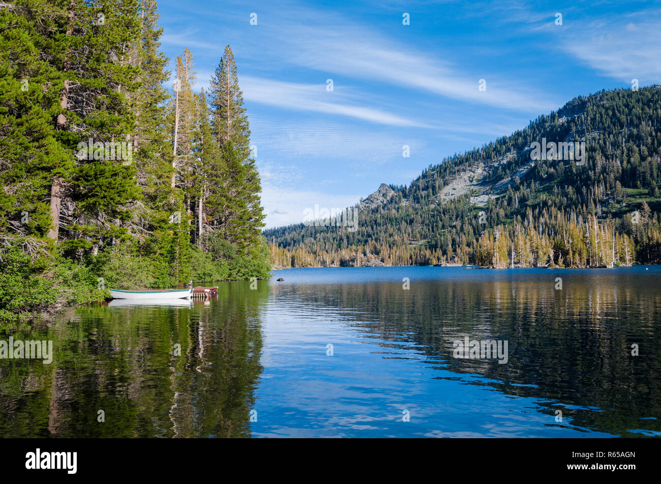 Barca bianca con rivestimento verde riflessa nella calma blue lago alpino legata a un litorale di alti pini in California della Sierra Nevada Foto Stock