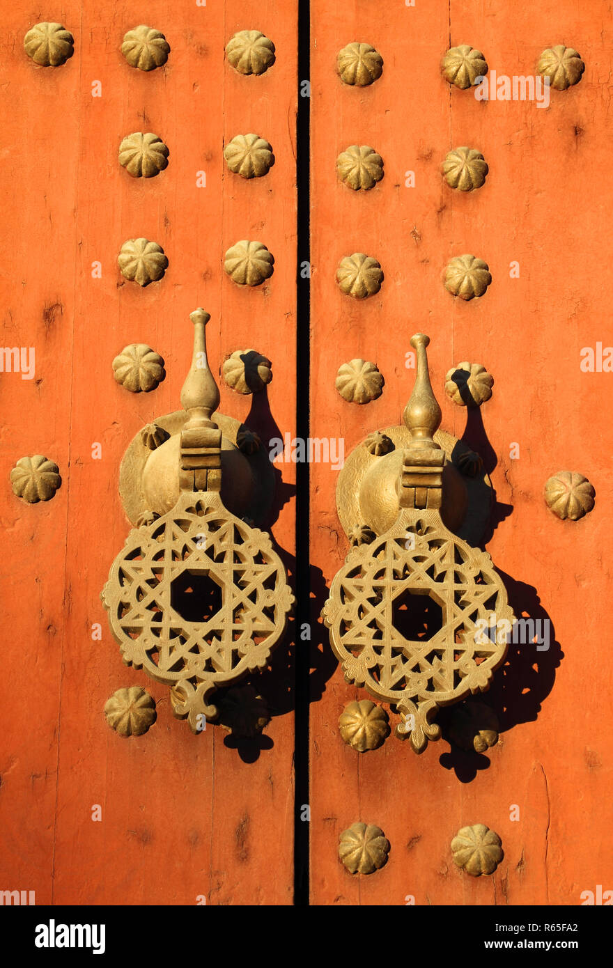 Tipico vecchio rustico di legno chiodati porta con modelli islamici su ottone doorknockers, Marocco. Foto Stock