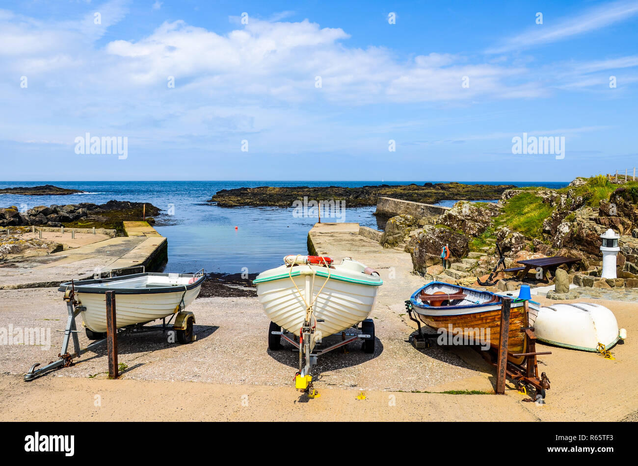 Una linea di tre colorata Vecchia legno barche da pesca tirato a riva di un piccolo porto sulla costa rocciosa dell'Irlanda del Nord a Porto Dunseverick Foto Stock